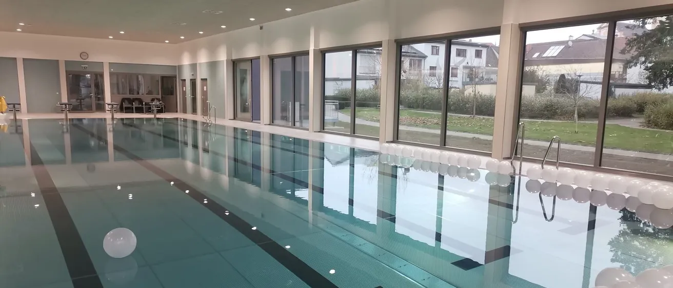 Ein sauberer, leerer Innenpool mit großen Fenstern, modernem Design und klarem blauem Wasser, umgeben von weißen Wänden und reflektierenden Fliesen.