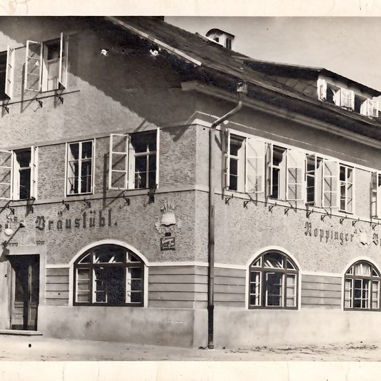 Ein Schwarz-Weiß-Foto aus alten Zeiten zeigt ein Gebäude mit dem Namen Braustube, mit Rundbogenfenstern, einem Schornstein und einem Schild an der Wand.