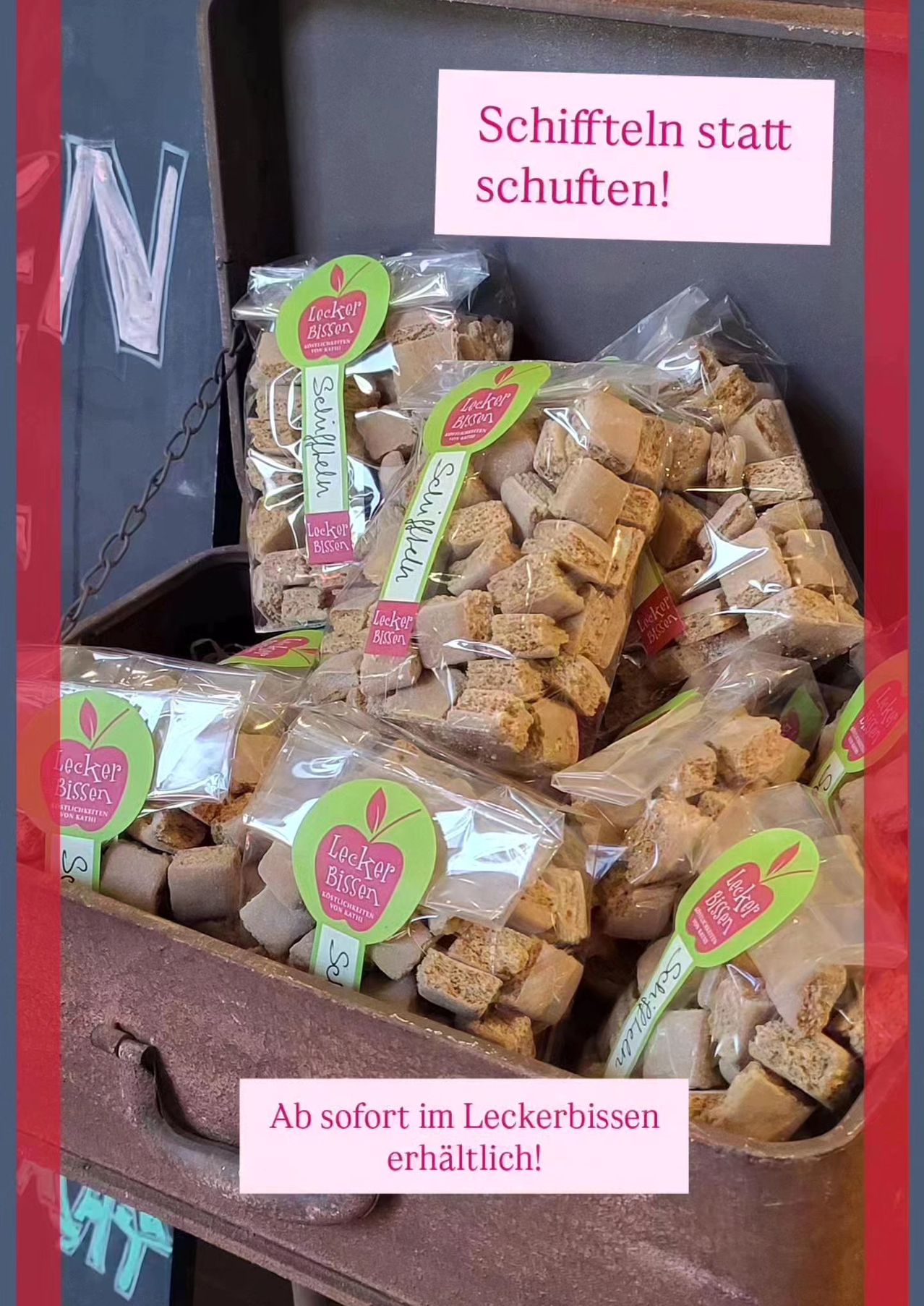 Pakete von Snack-Lebensmitteln in durchsichtigen Tüten, beschriftet mit 'Lekker Bissies', sind ordentlich in einem hölzernen Behälter mit rotem Rand gestapelt. Ein Schild über dem Behälter lautet 'schuitlen!'.