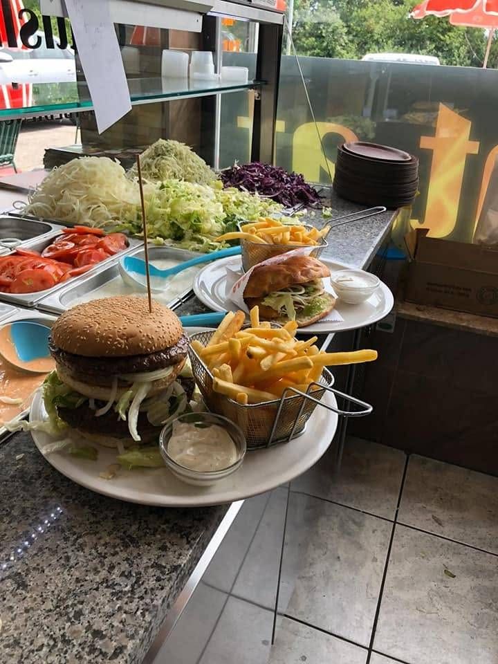 Ein Tresen mit einem großen Hamburger, Pommes und verschiedenen Beilagen auf einem weißen Teller präsentiert.