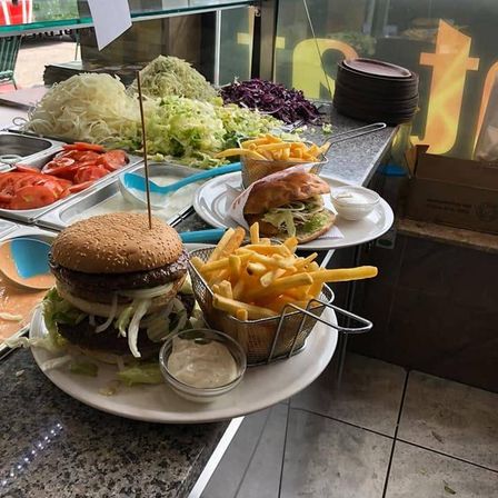 Ein Tresen mit einem großen Hamburger, Pommes und verschiedenen Beilagen auf einem weißen Teller präsentiert.