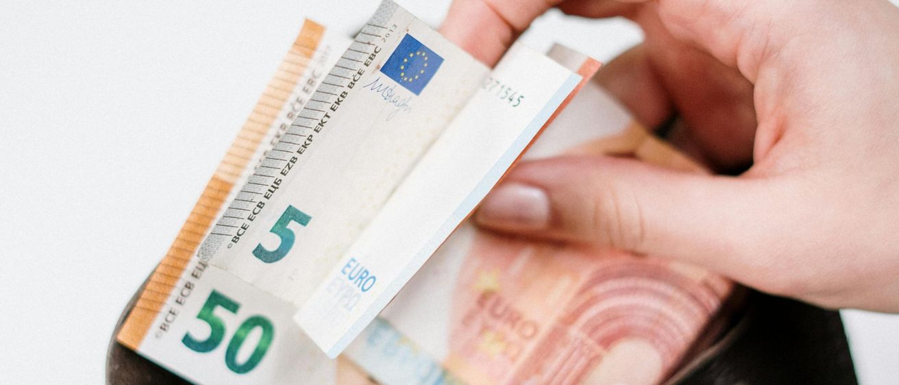 Eine Person öffnet einen braunen Geldbeutel und zeigt mehrere Euro-Banknoten, darunter eine 50-Euro-Note.
