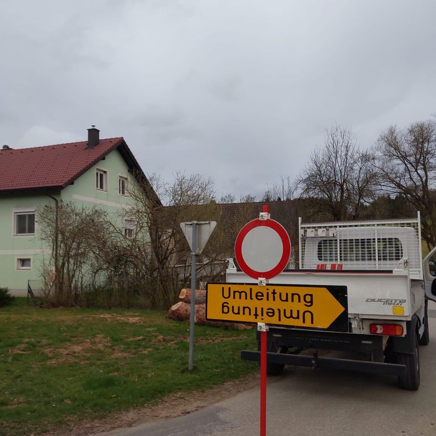 Ein weißer Pickup-Truck ist am Straßenrand geparkt, mit einem Schild, das auf eine Straßensperrung hinweist.
