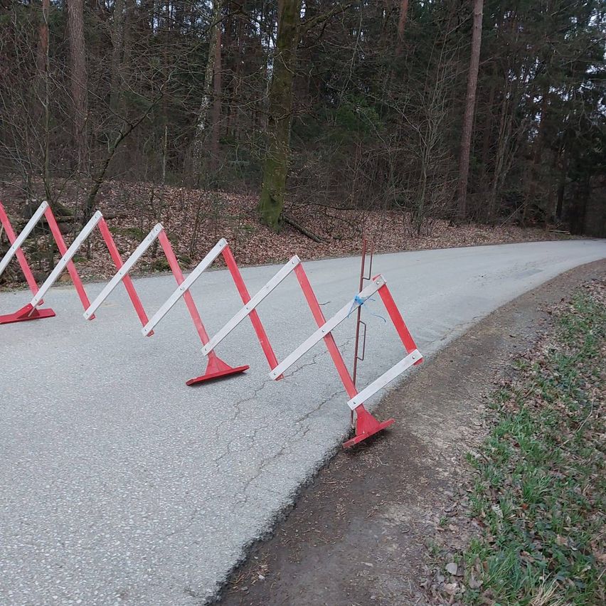 Eine Reihe roter und weißer Barrieren ist am Straßenrand aufgestellt, möglicherweise zur Wegblockade oder zur Signalisierung einer Gefahr.