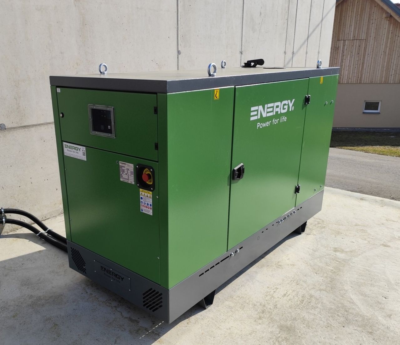 Ein großer grüner Energiegenerator, mit der Marke ENERGY, steht auf Beton. Er hat einen Monitor und verschiedene Aufkleber. Der Generator steht an einer Betonwand.