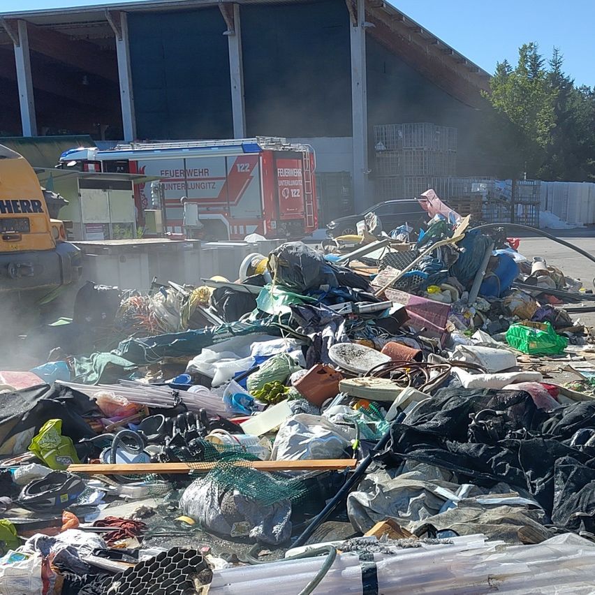 Ein Feuerwehrauto steht neben einem großen Haufen Müll und Schutt. Das Feuerwehrauto ist rot und weiß mit dem Wort 'Feuerwehr' an der Seite.