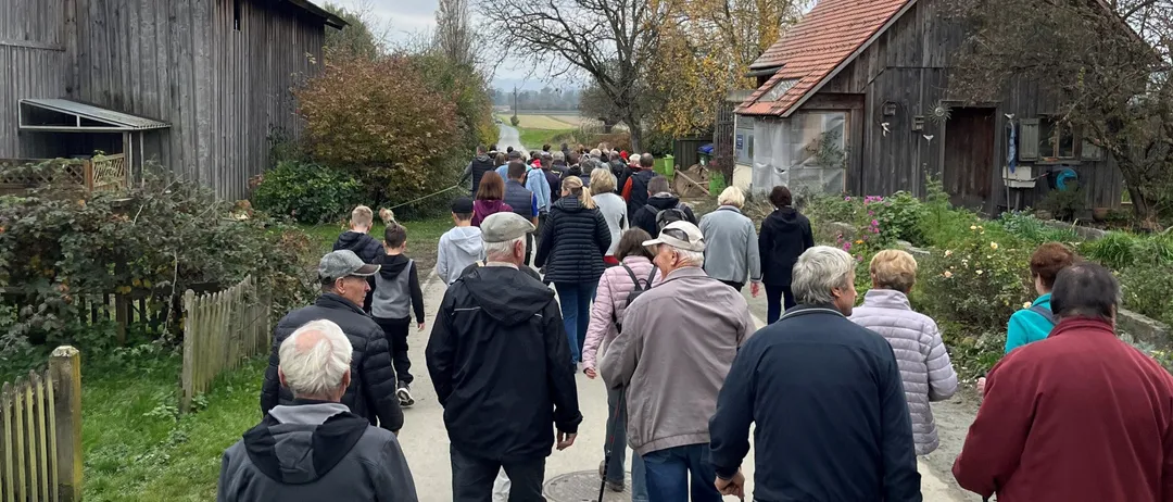 Eine Gruppe von Menschen geht auf einem Pfad vor einer Scheune.
