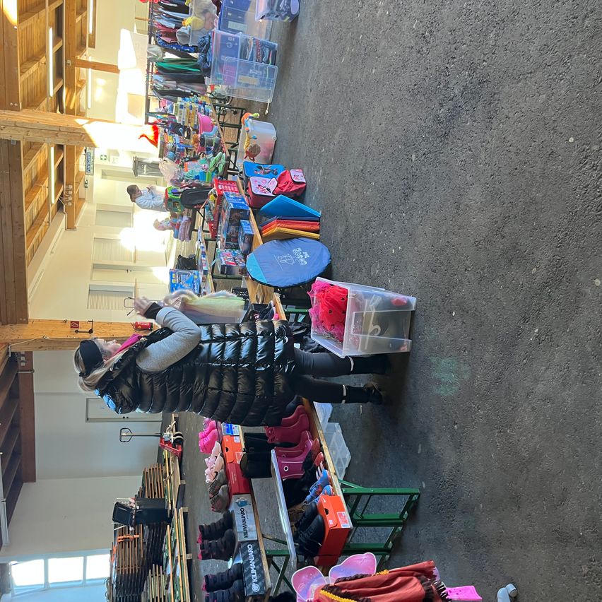 Eine Aufsichtsansicht eines Spendenzentrums mit vielen Gegenständen auf Tischen. Eine Frau in einer gepolsterten Jacke hält einen Plastikbehälter. Hinter ihr sortieren Menschen verschiedene Gegenstände.
