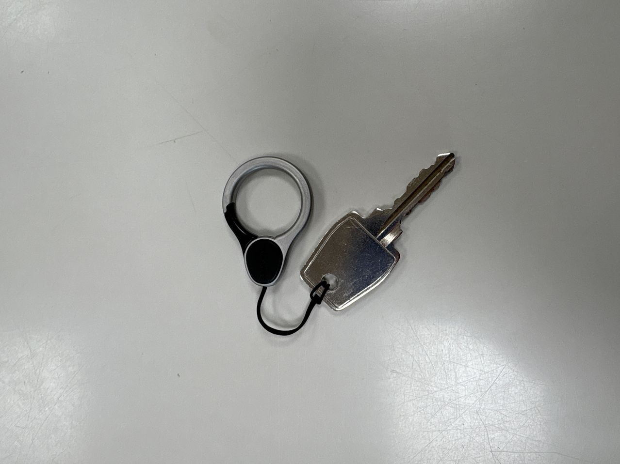 Ein silberner Schlüssel mit schwarzem Griff ist an einem silbernen Ring auf einer weißen Oberfläche befestigt.