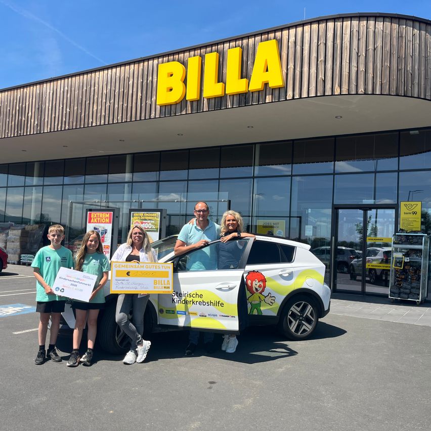 Fünf Personen posieren vor einem BILLA-Geschäft mit einem Auto. Sie halten einen Scheck und eine Schachtel. Das Auto hat einen Aufkleber und das Wort Kinderkrebshilfe an seiner Tür.