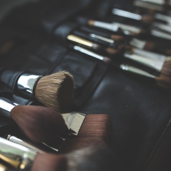 Eine Sammlung von Make-up-Pinseln in einem schwarzen Lederetui, in Reihen angeordnet. Einige Pinsel sind verschwommen, und einige haben glänzende Griffe.