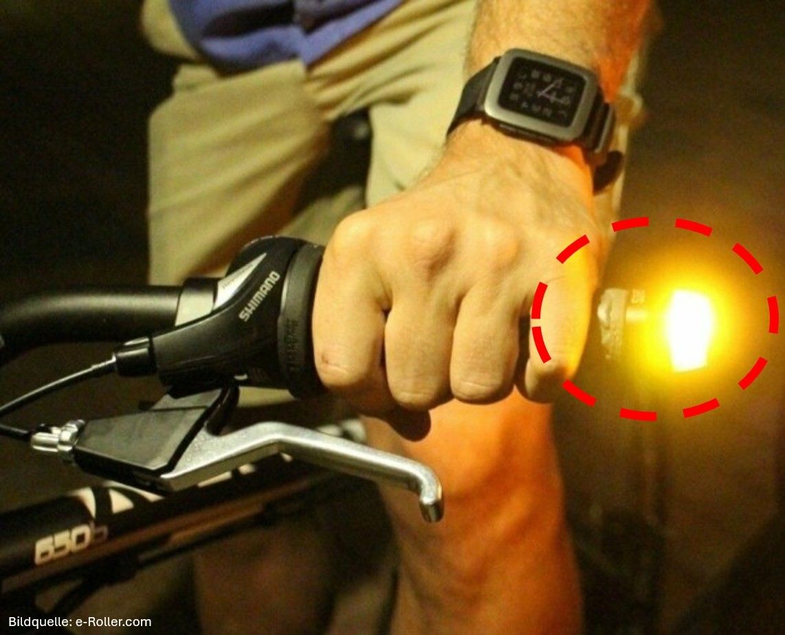 A close-up of a cyclist's hand on a bike brake lever with a lit light. The light is highlighted with red circles.