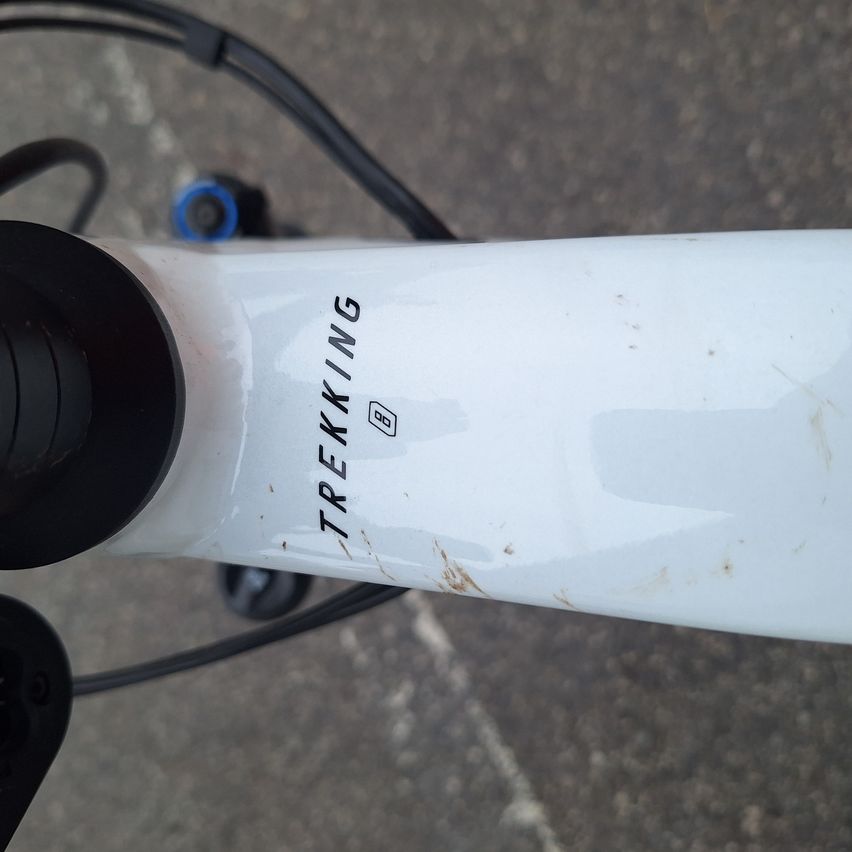 A close-up of a white bicycle frame with 'TREKING' and '00' printed on it. Some dirt and scratches are visible.