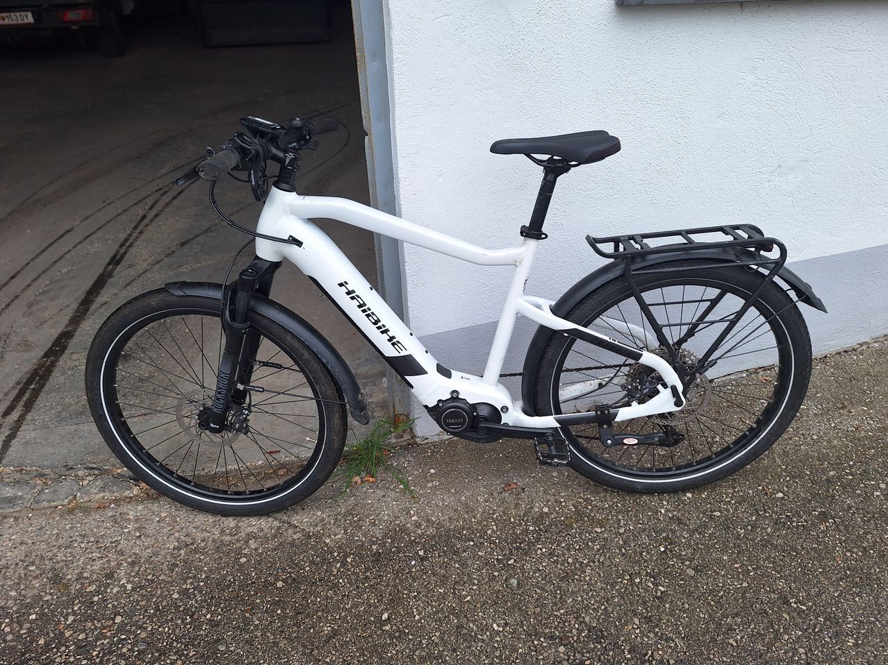 A white electric bicycle with a black seat, handlebar, and wheels is parked outside. It has a black rear rack.