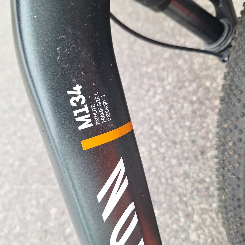 Close-up of a bicycle's frame displaying 'M134', 'PATLITE', 'ATHLETE SIZE', 'FRAME CATEGORY 1', and a black and orange strip.