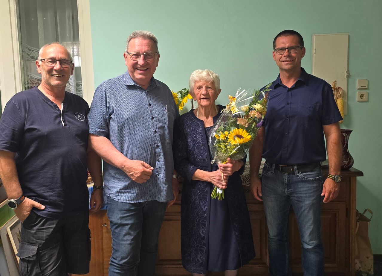 Geburtstagsfeier: Frau mit Blumenstrauß und drei Männern in einem Wohnzimmer