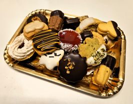 Ein goldenes Tablett hält eine Vielfalt von Desserts, darunter Schokoladen-Donuts, herzförmige Kekse und Sahnepuffs mit verschiedenen Toppings.