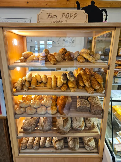 Eine Holzvitrine gefüllt mit verschiedenen Brotsorten. Das oberste Regal hat Brötchen und Semmeln, die Mitte hat Baguettes und das unterste hat verschiedene Brote.