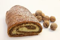Ein Walnussstrudel mit sichtbarem Querschnitt, gefüllt mit Sahne und mit Puderzucker bestreut. Daneben liegen einige Walnüsse.
