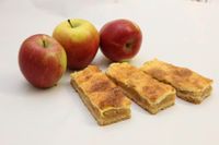 Drei Apfelscheiben, eine gelb und zwei rot, sind mit Apfelstangen auf einer weißen Oberfläche zu sehen. Die Apfelstangen haben eine knusprige obere Schicht.