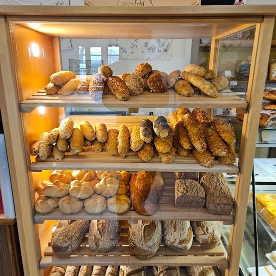 Eine Vitrine mit verschiedenen Brotsorten, darunter Baguettes, Brötchen und Laibe, unter warmer Beleuchtung.