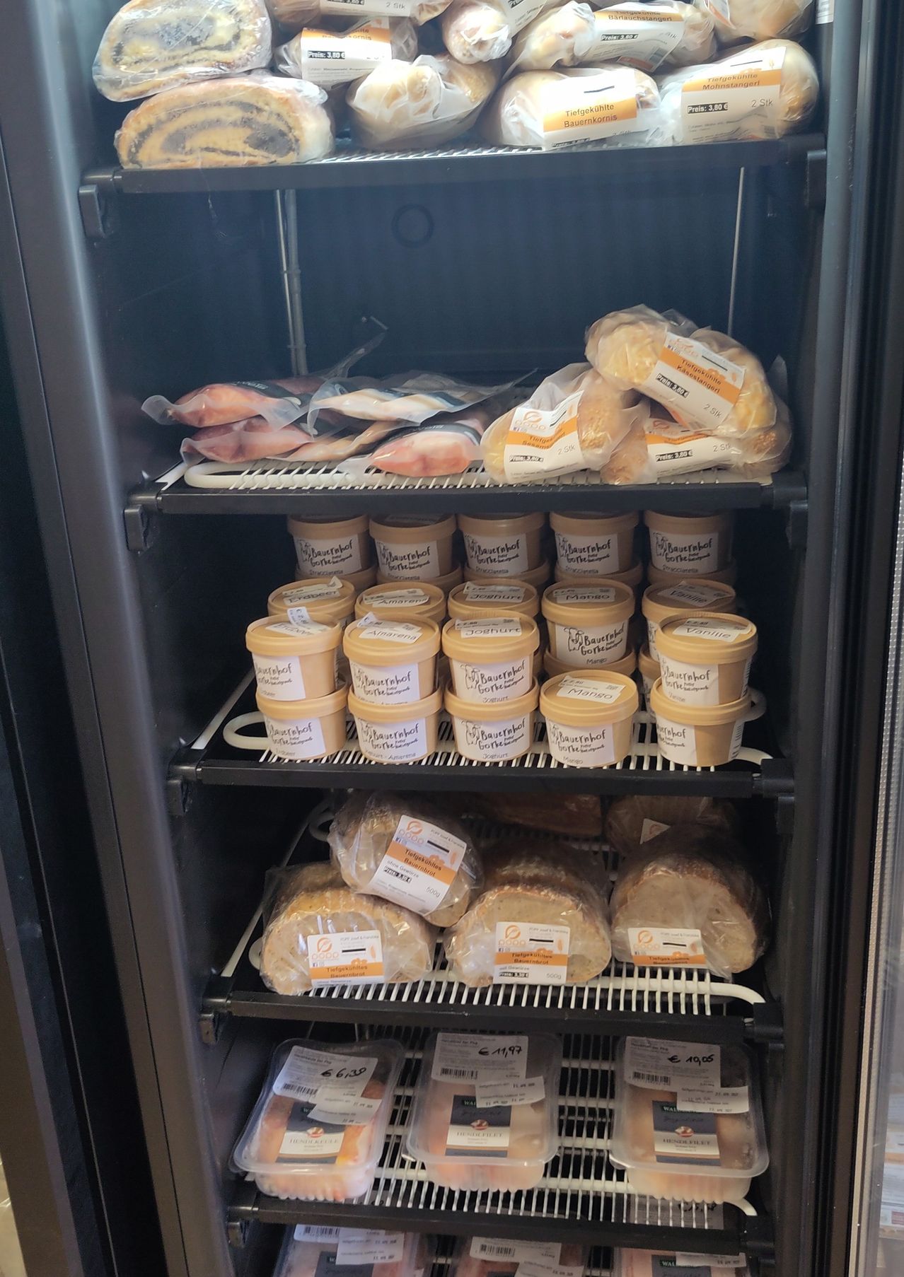 Ein Kühlschrank gefüllt mit verschiedenen Produkten, einschließlich Brot, Brötchen und Behältern mit Butter. Die Produkte sind auf mehreren Regalen platziert.
