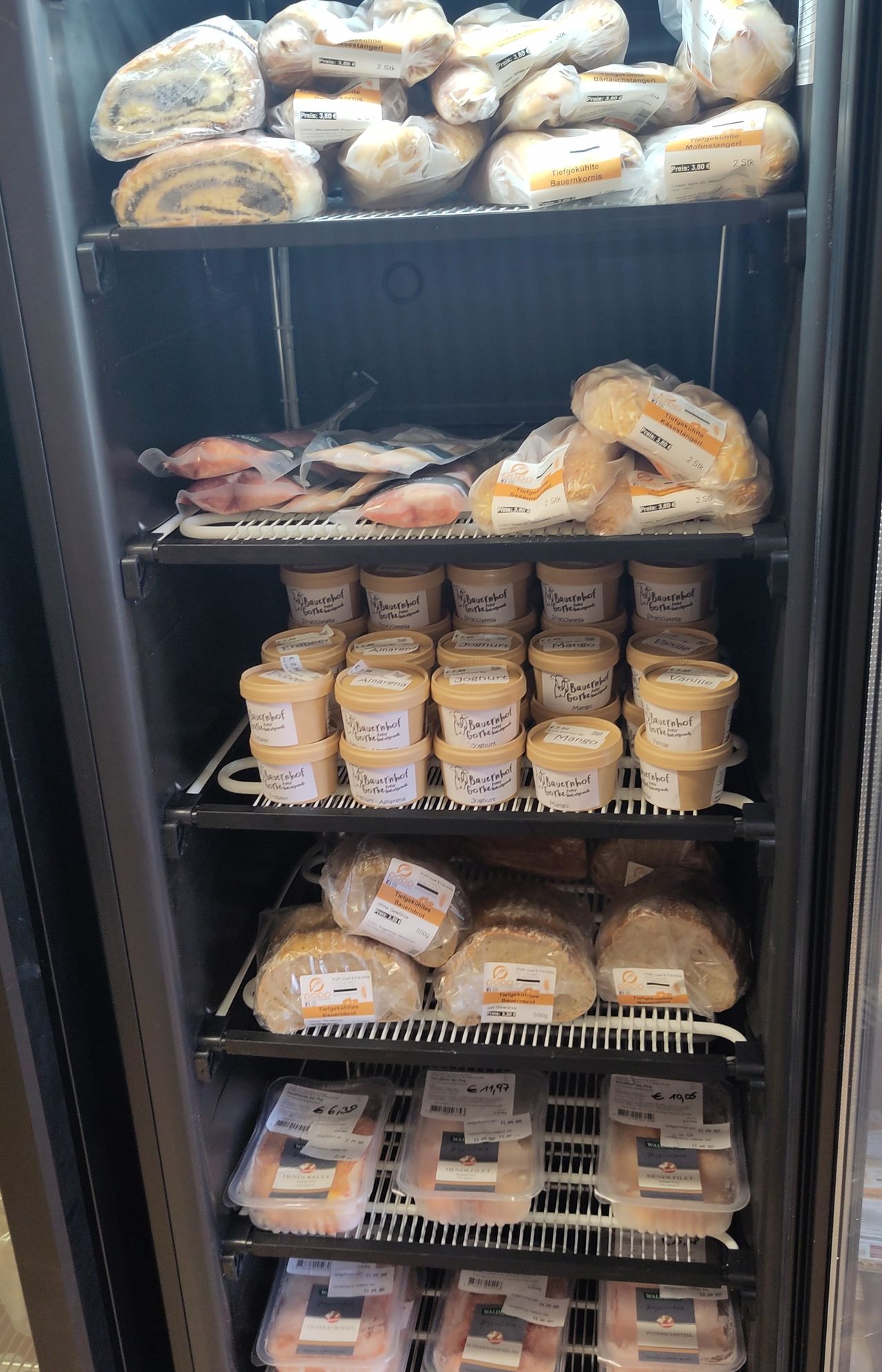 Ein Kühlschrank gefüllt mit verschiedenen Produkten, einschließlich Brot, Brötchen und Behältern mit Butter. Die Produkte sind auf mehreren Regalen platziert.