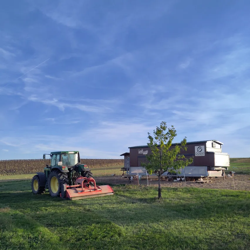 Ein Traktor steht auf einem grünen Feld mit einem kleinen Haus im Hintergrund.