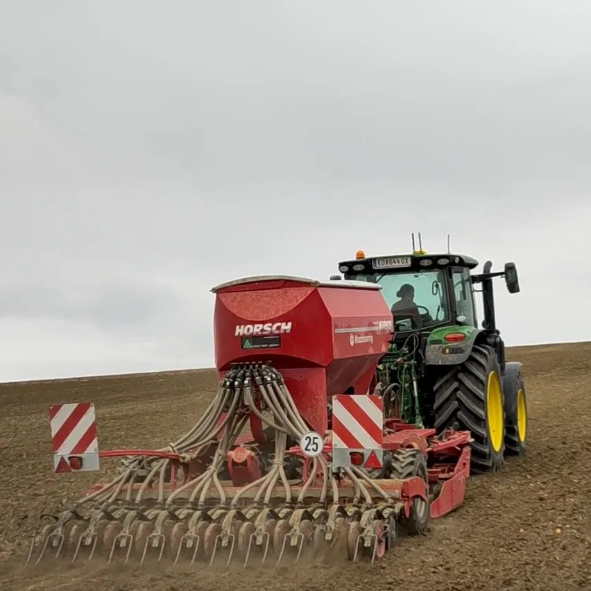 Ein roter Traktor mit einem großen roten Sämaschinenanbau pflüget ein Feld. Der Traktor hat die Nummer 25 an seiner Seite.