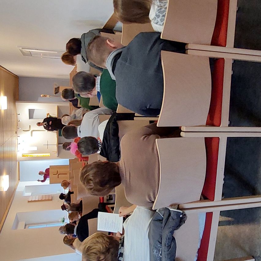 Eine Ansicht von oben eines Raumes, in dem Menschen in Reihen sitzen, wahrscheinlich während eines Gottesdienstes, mit einigen Personen, die vorne stehen.