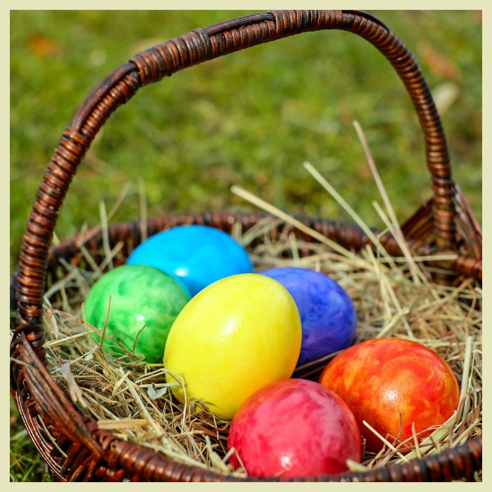 Ein Korb aus Weide liegt mit bunten Ostereiern auf einem Grasfeld. Die Eier sind in verschiedenen leuchtenden Farben wie Blau, Grün, Gelb, Rot und Orange.