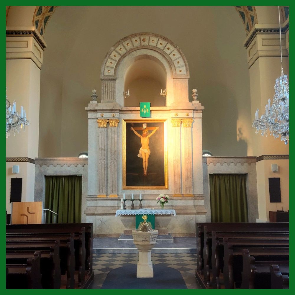 An interior view of a church with a large painting of Jesus on the cross above the altar, surrounded by candles and flowers.