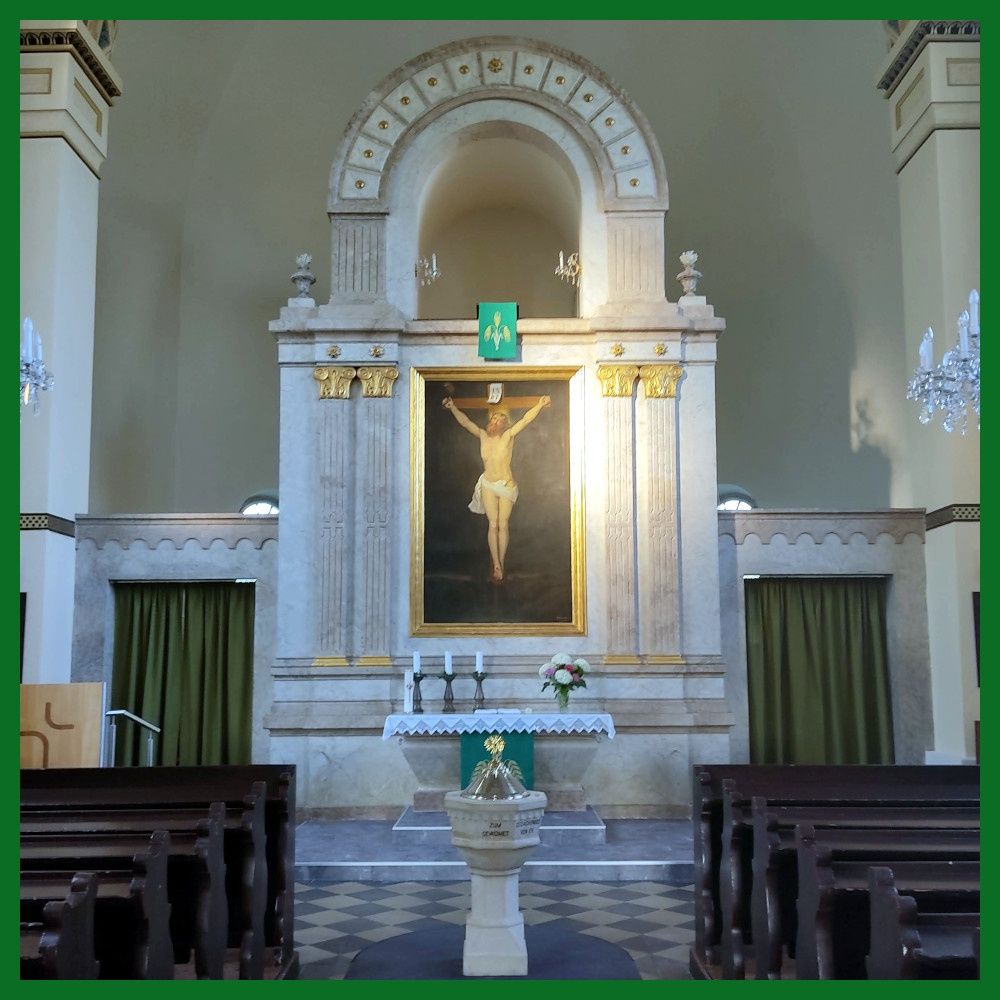 Ein Altar in einer Kirche mit einem großen Gemälde von Jesus am Kreuz, flankiert von zwei Kerzen, und einem kleinen Tisch mit Blumen.