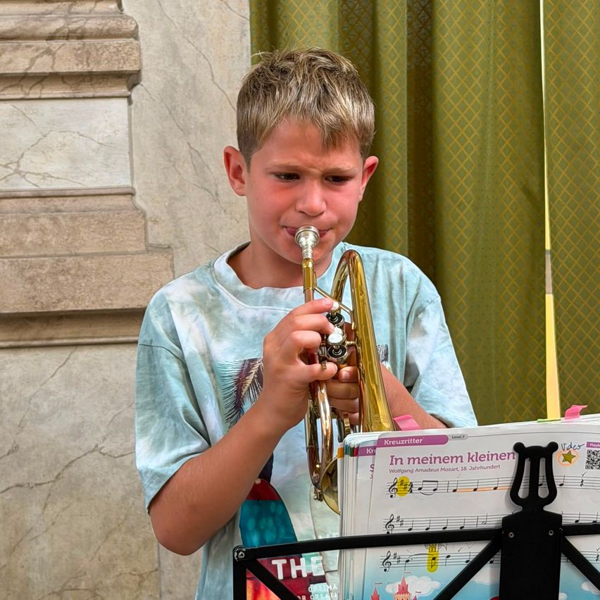 Ein junger Junge spielt Trompete vor einem Notenständer mit einem Blatt Musik mit dem Titel 'In meinem kleinen'.