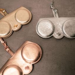 Drei metallische Geldbörsen in Gold, Silber und Roségold liegen auf einer grauen Oberfläche. Jede Geldbörse hat zwei kreisförmige Fächer mit einem Sterndesign in der Mitte.