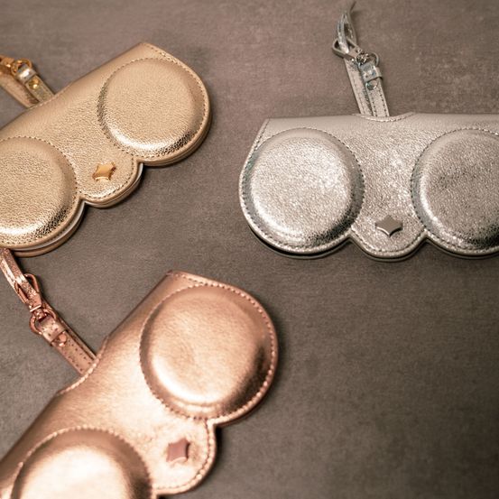 Drei metallische Geldbörsen in Gold, Silber und Roségold liegen auf einer grauen Oberfläche. Jede Geldbörse hat zwei kreisförmige Fächer mit einem Sterndesign in der Mitte.