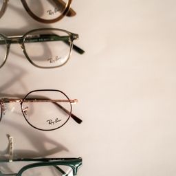 Vier Brillen mit grünen Rahmen und goldenen Rändern sind in einer Reihe auf einer weißen Oberfläche angeordnet. Die Rahmen tragen den Namen Ray-Ban auf der Innenseite.