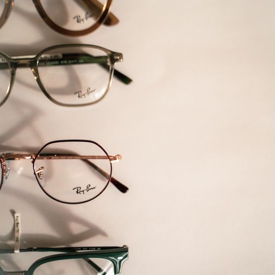 Vier Brillen mit grünen Rahmen und goldenen Rändern sind in einer Reihe auf einer weißen Oberfläche angeordnet. Die Rahmen tragen den Namen Ray-Ban auf der Innenseite.