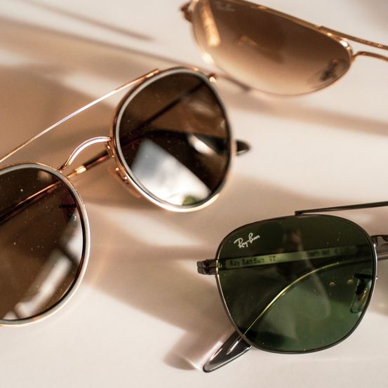 Drei Paar Ray-Ban-Sonnenbrillen liegen auf einer weißen Oberfläche. Die Sonnenbrillen haben grüne Gläser und goldene Rahmen.