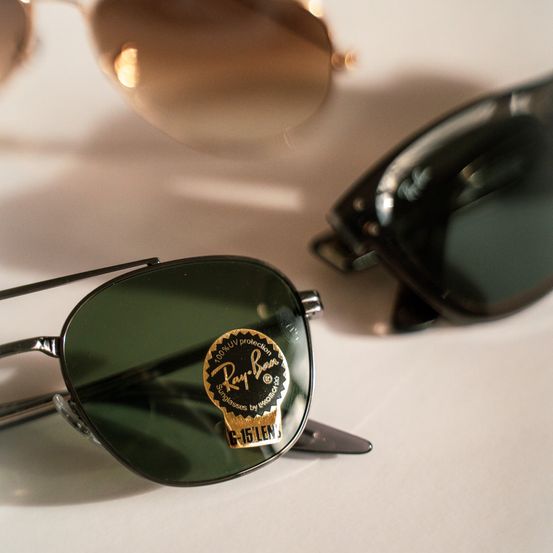 Ein Nahaufnahme von drei Sonnenbrillen, darunter ein Paar mit einem Ray-Ban-Logo auf der Linse.