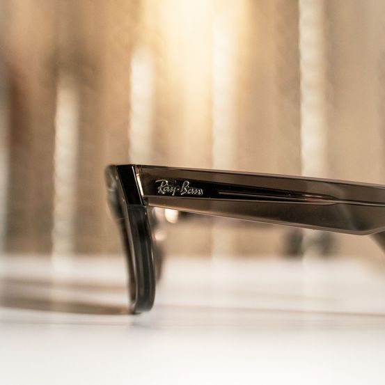 Eine Nahaufnahme von schwarzen Ray-Ban-Brillen mit goldener Markenschrift. Der Hintergrund ist unscharf.