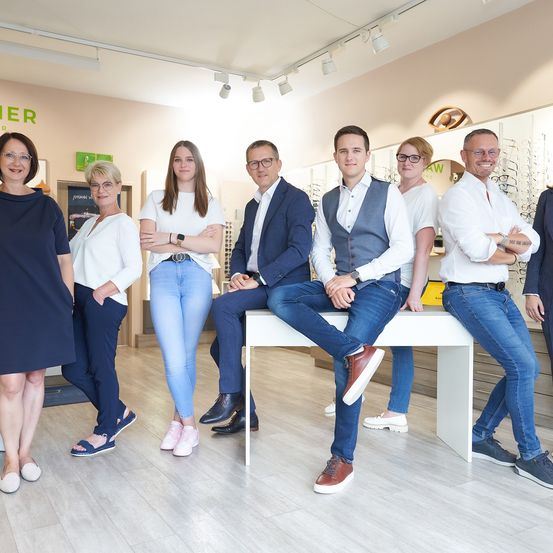 Eine Gruppe von Menschen posiert für ein Foto in einem Geschäft. Vier Männer und drei Frauen stehen und sitzen. Dahinter befinden sich Regale mit Artikeln.