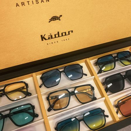 Eine Schachtel mit Sonnenbrillen der Marke 'Kador', gegründet 1962, wird gezeigt. Verschiedene Paar Sonnenbrillen sind in den Fächern der Schachtel zu sehen.