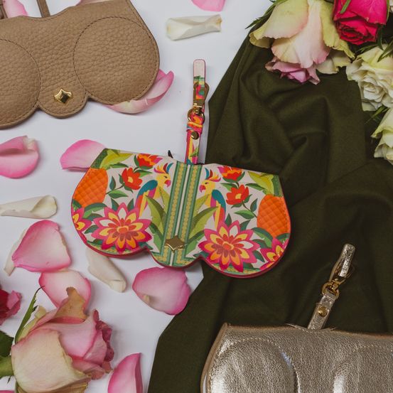 A vibrant floral print clutch, brown and silver handbags, and rose petals are laid out on a white surface.