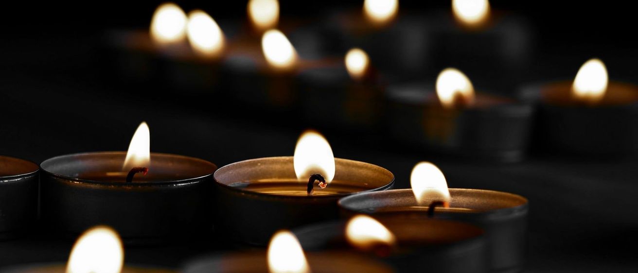 Mehrere Kerzen in einem schwach beleuchteten Raum brennen und werfen sanftes gelbes Licht. Die Kerzen sind ordentlich in Reihen angeordnet.