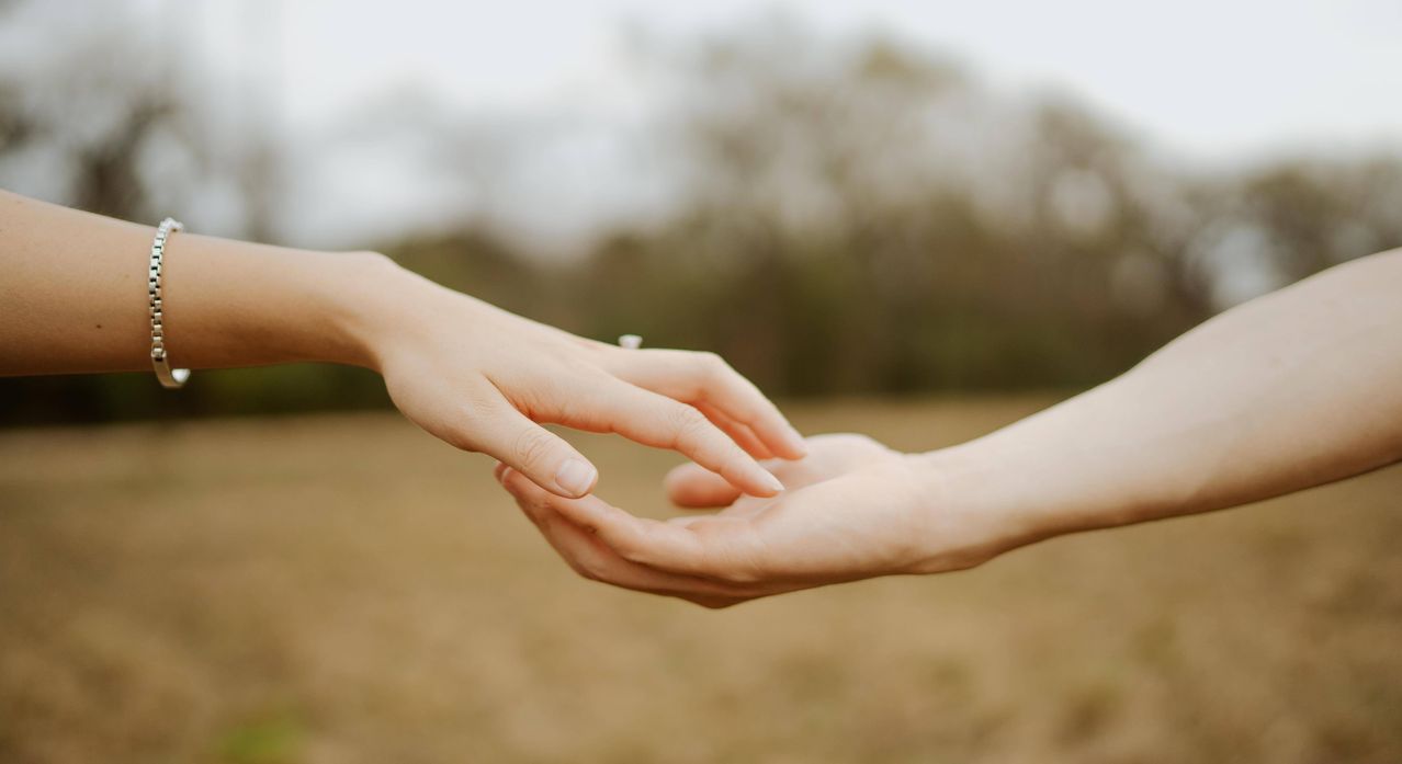 Zwei Hände halten sich in einem Außenbereich. Eine Hand ist leicht erhoben und scheint der anderen einen Heiratsantrag zu machen.
