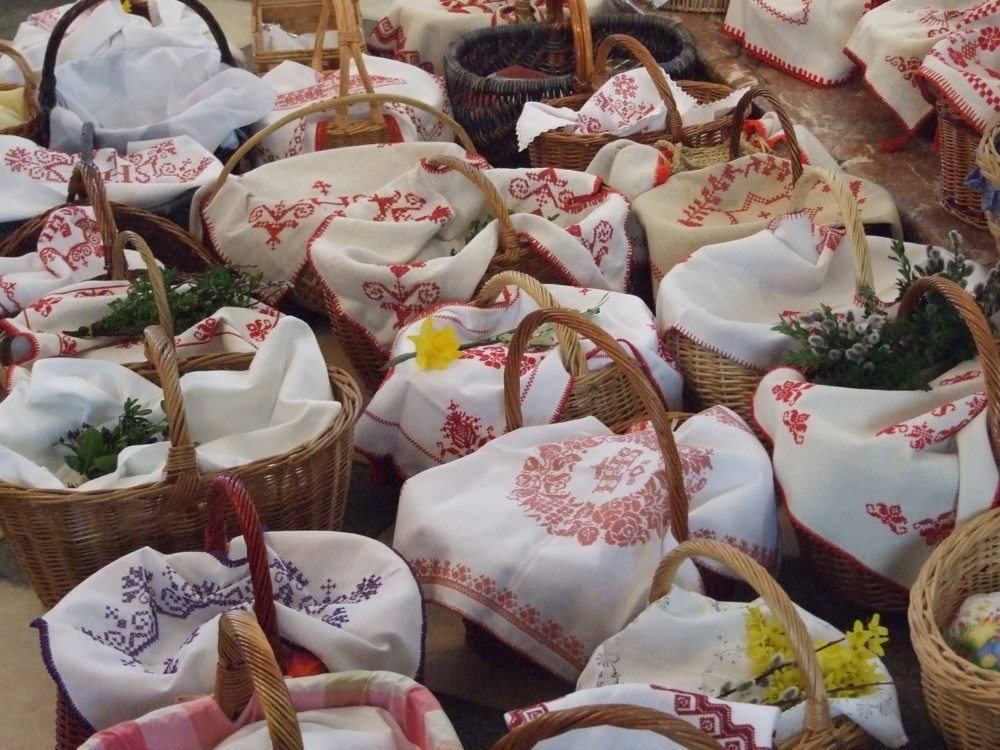 Verschiedene Weidenkörbe gefüllt mit Blumen und Kräutern sind gestapelt. Jeder Korb hat einen weißen Stoff mit roten Stickereien darauf.