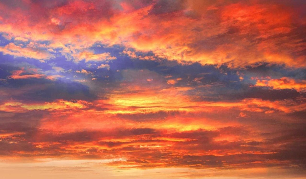 A sunset with clouds painted in vibrant hues of orange, red, and purple, with a gradient to lighter blue in the distance.