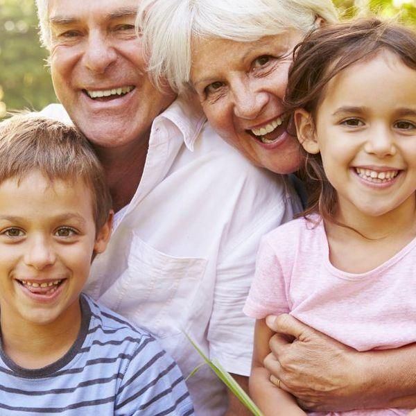 Eine lächelnde drei Generationen umfassende Familie, bestehend aus Großvater, Großmutter und ihren Enkelkindern, die gemeinsam in einem Park posieren.
