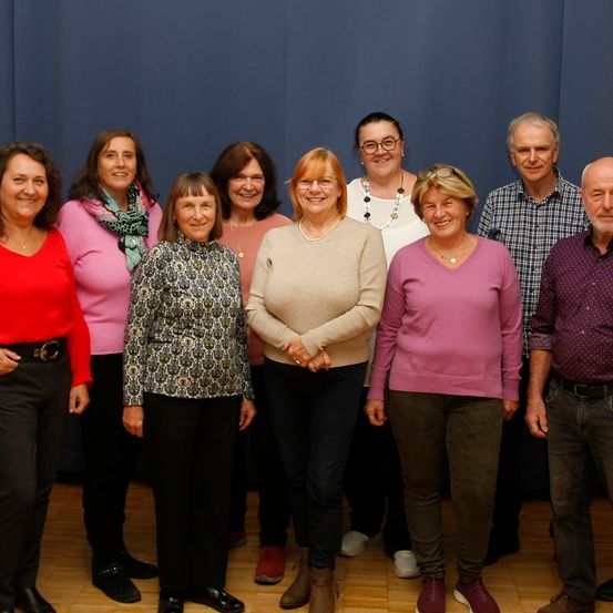 Eine Gruppe von Erwachsenen, sowohl Männer als auch Frauen, stehen für ein Foto zusammen. Sie alle lächeln und scheinen für ein Bild zu posieren. Die Frau auf der rechten Seite trägt eine Brille.